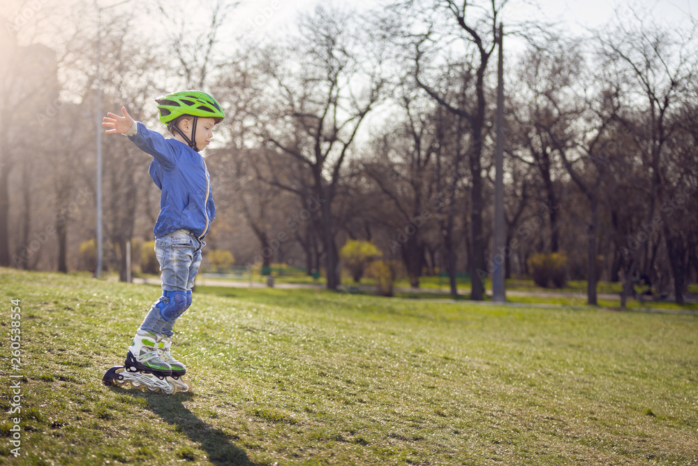 Cute boy in the park rides on the rollers. Sunny and warm.