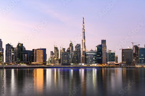 Panoramic view of the illuminated Dubai skyline during sunset with the magnificent Burj Khalifa and many others skyscrapers reflected on a silky smooth water flowing in the foreground. Dubai.