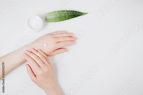 Top view woman putting nutritious cream on her hands on white background among jar of cosmetic cream, Aloe vera fresh leaves. Moisturizing cream for clean and soft skin. Healthcare concept.