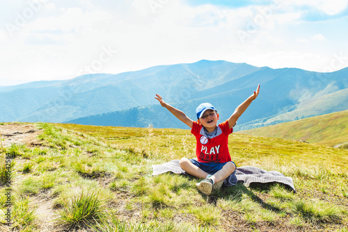 little boy sitting on blanket on peak of mountain. beautiful landscape on background