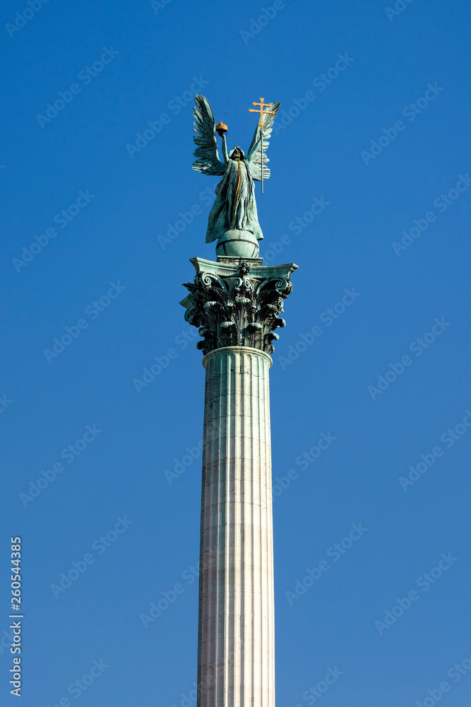 Hungary, Budapest, Hosok tere: Close up detail view famous column with Archangel Gabriel at Heroes' Square in the city center of the Hungarian capital with column, people, blue sky in the background. Hungary, Budapest, Hosok tere: Close up detail view famous column with Archangel Gabriel at Heroes' Square in the city center of the Hungarian capital with column, people, blue sky in the background.