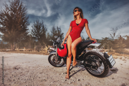 Obraz na płótnie Outdoor lifestyle portrait of young sexy woman in red swimsuit sitting on a vintage custom motorcycle w salonie