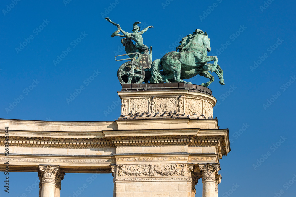Hungary, Budapest, Hosok tere: Statue Man with a Snake as symbol of War on top of left colonnade at famous Heroes' Square in the sunny city center of the Hungarian capital with blue sky in background.