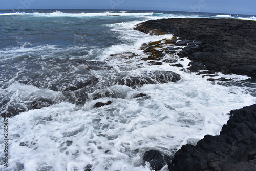 Waves Crashing on Rocky Shore in Hawaii white foam as the waves wash over the rocks under a blue sky