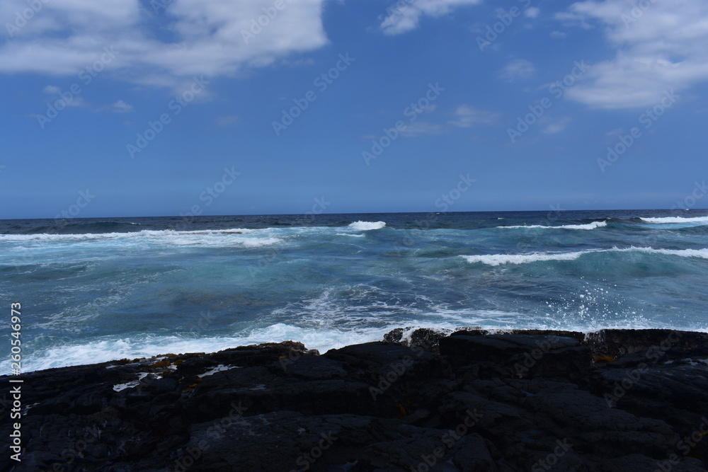 Waves Crashing on Rocky Shore in Hawaii white foam as the waves wash over the rocks under a blue sky Waves Crashing on Rocky Shore in Hawaii white foam as the waves wash over the rocks under a blue sky