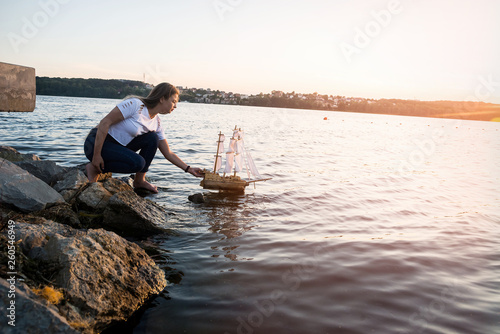 Beautiful woman sailing toy ship on water