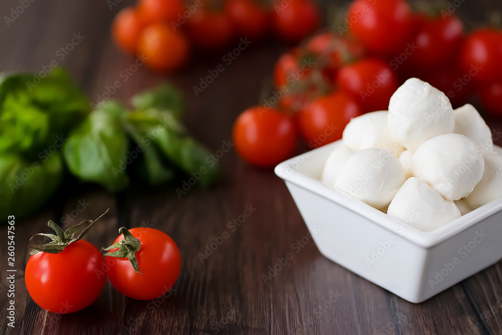 Mozzarella cheese, basil and cherry tomatoes on  brown wooden table. Ingredients for making salad caprese. Mediterranean Kitchen.