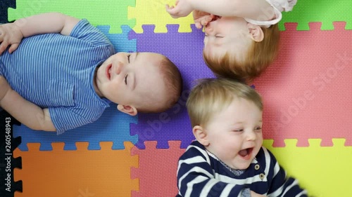 Overhead View Of Babies Lying On Mat At Nursery PlaygroupBeing Tickled By Mothers And Laughing