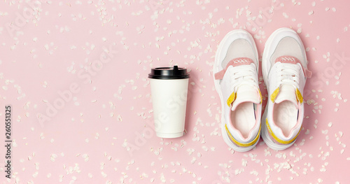 Female Fashionable Sneakers, Coffee or tea paper cup and spring branches of white flowers on pink background top view flat lay. Take away coffee cup, mockup. Creative spring background, lifestyle
