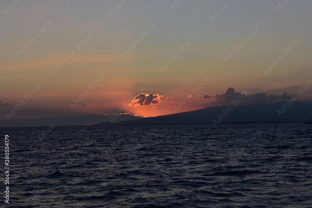 Fototapeta premium Bright sky at sunset over the Pacific Ocean in Hawaii Sun dipping behind mountain and cloud throwing all sorts of colors into the sky