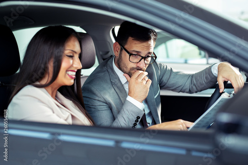 Attractive saleswoman showing inside of a car to customer