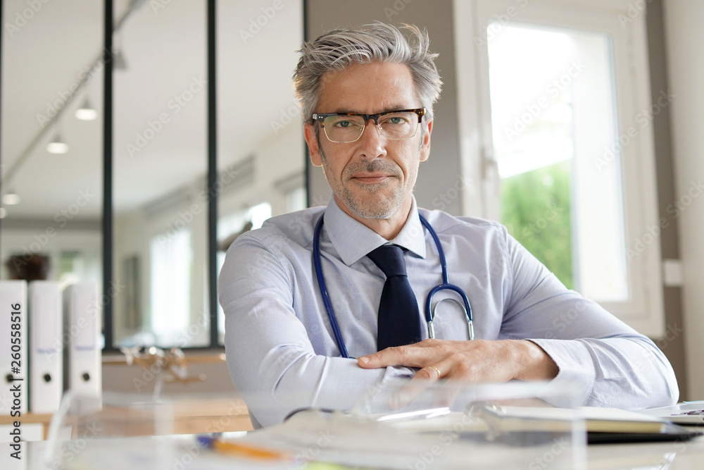 Fototapeta premium Mature doctor working in office looking at camera