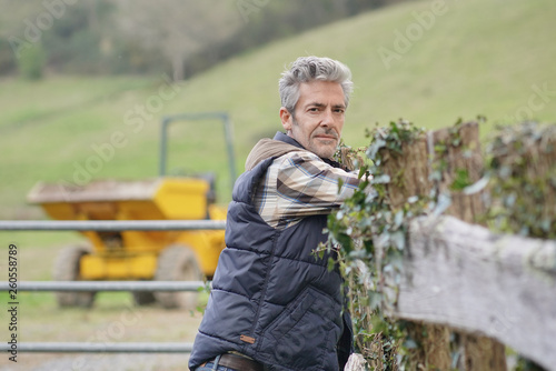Attractive farmer leaning on fence looking at camera