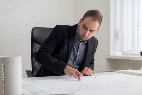 Businessman in the office is looking closely into the blueprint of a modern house