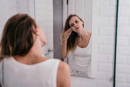 young woman reflected in the bathroom to see wrinkles on her face