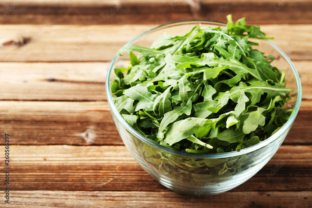 Green arugula leafs in glass bowl on brown wooden table Green arugula leafs in glass bowl on brown wooden table
