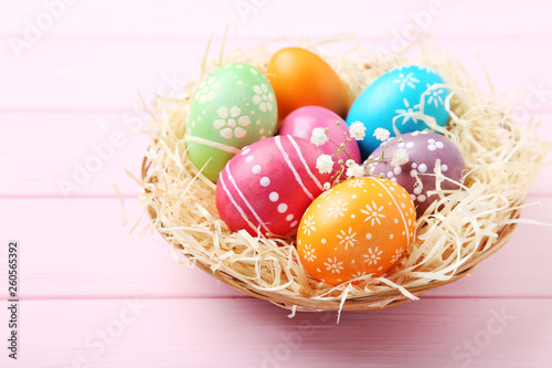 Colorful easter eggs in basket on pink wooden table