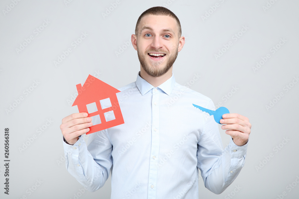 Young man with paper house and key on grey background Young man with paper house and key on grey background