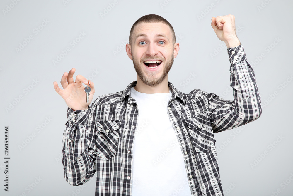 Young man holding silver key on grey background Young man holding silver key on grey background