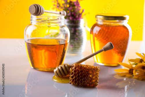Honey dripping from a wooden honey dipper in a jar on wooden background