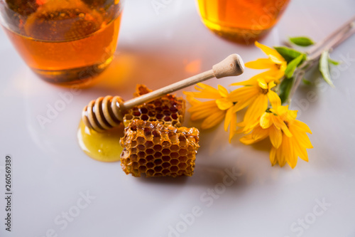 Honey dripping from a wooden honey dipper in a jar on wooden background