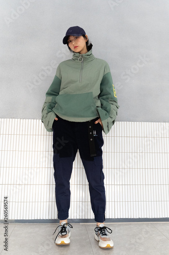 Asian girl weaing a large green jacket with sports shoes, black pants ,looking sharp and cool