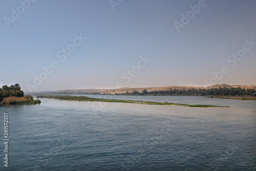 Blick auf den Nil in Ägypten nahe Luxor mit Pflanzen am Ufer und Wüste im Hintergrund