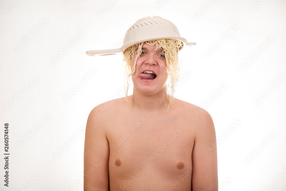 A young, fat, cheerful, smiling boy with a colander and spaghetti noodles on his head. Plump body without clothing. White background. Portrait photo. A young, fat, cheerful, smiling boy with a colander and spaghetti noodles on his head. Plump body without clothing. White background. Portrait photo.