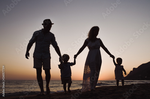 A family with two toddler children walking on beach on summer holiday at dusk.