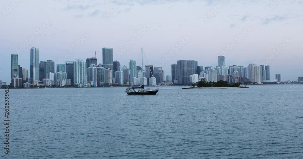 Left pan shot of the Brickell skyline at dawn with the blue sky reflecting on the ocean and the boats swaying from the waves and Isla Neira becoming visible as birds fly by. 4k Left pan shot of the Brickell skyline at dawn with the blue sky reflecting on the ocean and the boats swaying from the waves and Isla Neira becoming visible as birds fly by. 4k