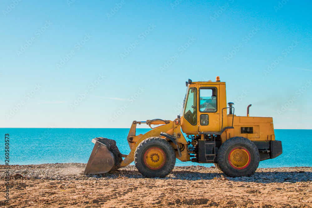 Yellow bulldozer on the background of clear blue sky and seashore. Copy space. Skyline Yellow bulldozer on the background of clear blue sky and seashore. Copy space. Skyline