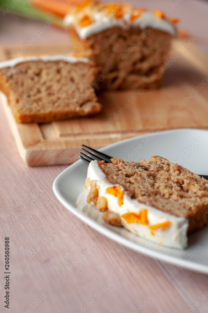 Loaf of carrot cake with cream cheese frosting and candy garnish on wooden table