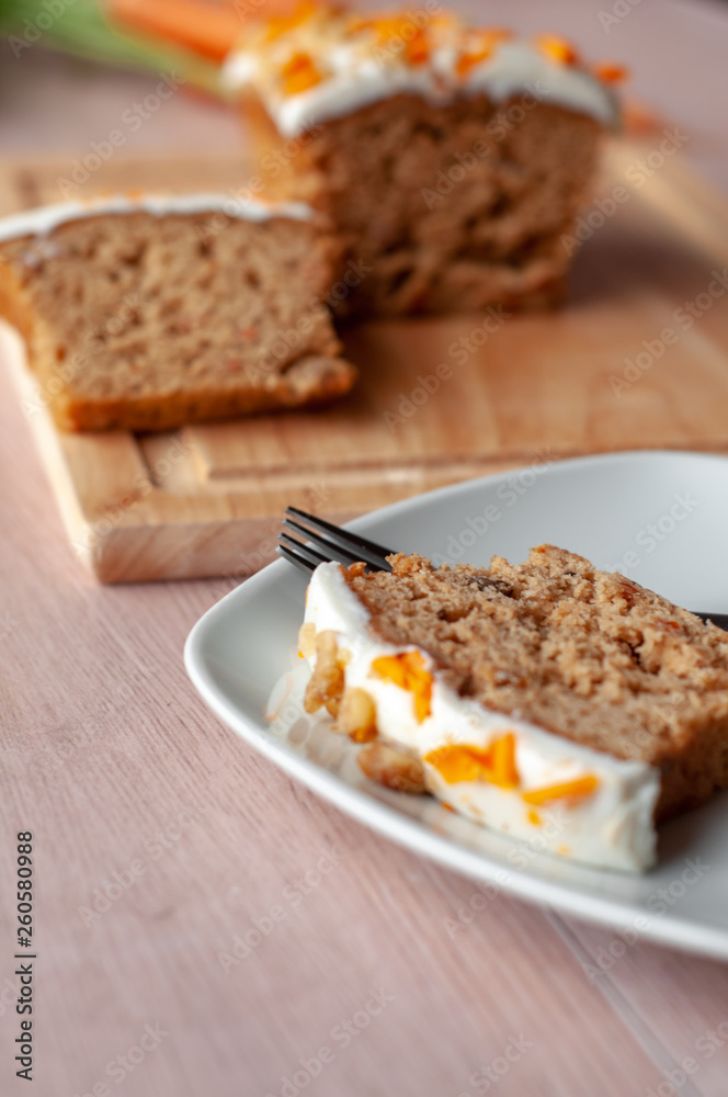 Loaf of carrot cake with cream cheese frosting and candy garnish on wooden table Loaf of carrot cake with cream cheese frosting and candy garnish on wooden table
