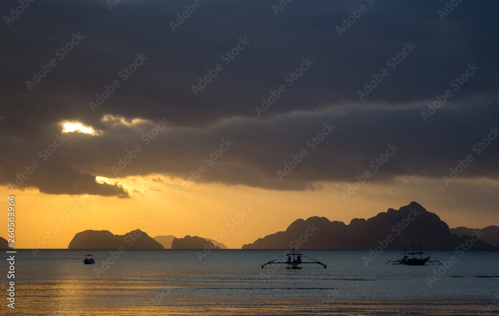 Boats silhouette in the sea on sunset and isles background. Traditional Philippines fishing boat at sunset. Scenic evening sky above sea. Travel and transport concept. Calm evening in tropical resort.