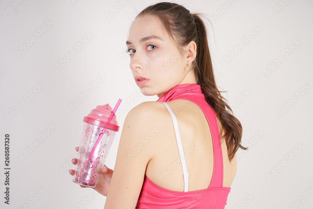 young beautiful caucasian teen girl in a pink short topic with a glass of water after training on a white background in the Studio young beautiful caucasian teen girl in a pink short topic with a glass of water after training on a white background in the Studio