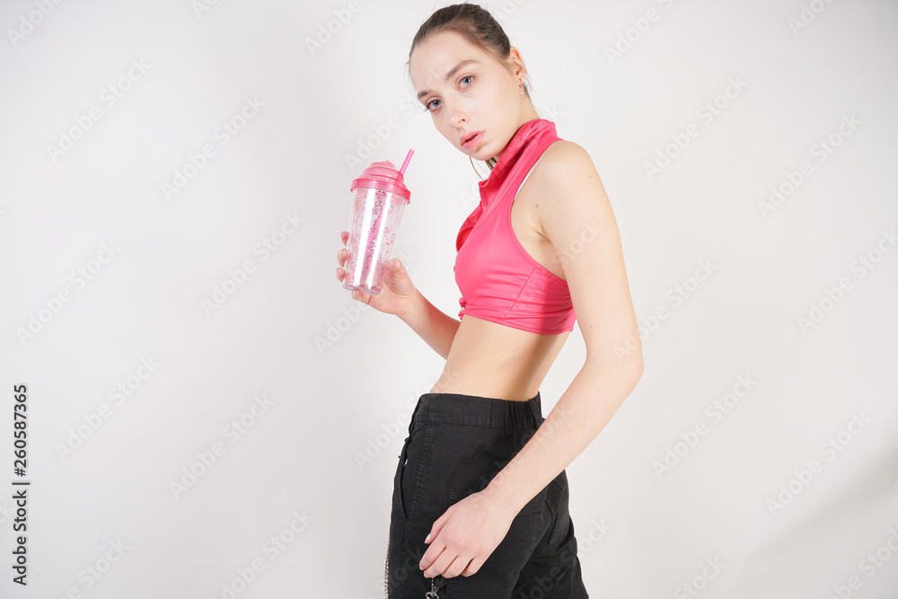 young beautiful caucasian teen girl in a pink short topic with a glass of water after training on a white background in the Studio young beautiful caucasian teen girl in a pink short topic with a glass of water after training on a white background in the Studio
