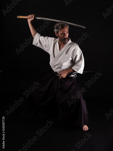 Aikido and Kenbudo practitioner with traditional costume on black background with katana sword