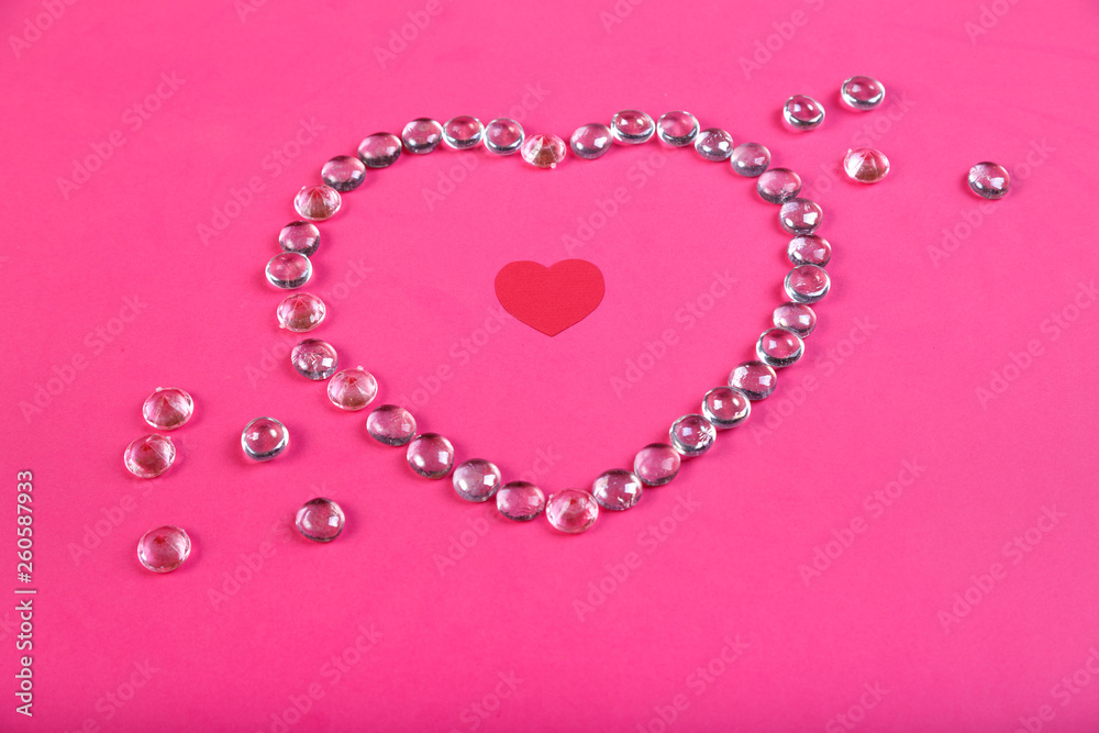 A heart lined with beads on a pink background with a heart in the middle in a frame of beads.