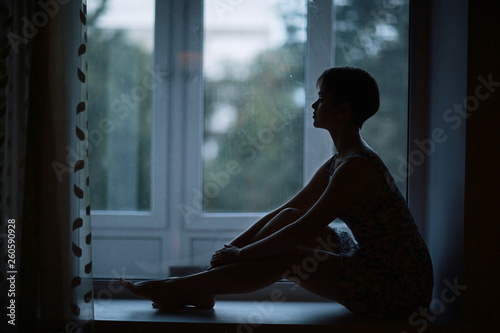 Silhouette of a dreamy girl sitting on a window photo