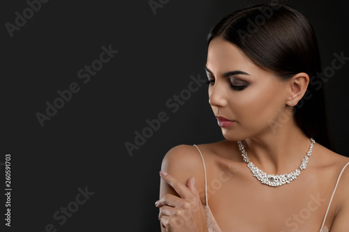 Beautiful young woman with elegant jewelry on dark background. Space for text