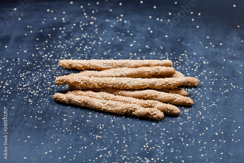 Italian grissini or salted bread sticks with sesame seeds on black board background.