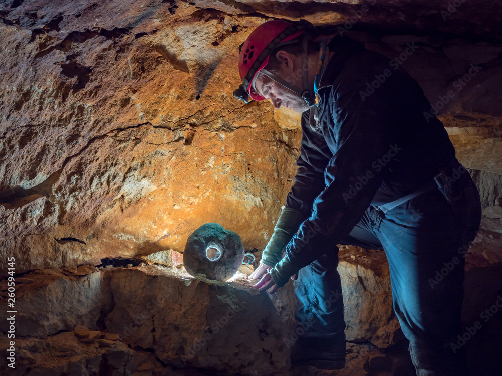 archaeologist look at the stone wheel illuminated by backlight  in the caves