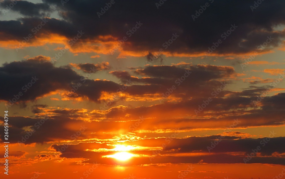 Beautiful fiery orange sunset background with dark clouds