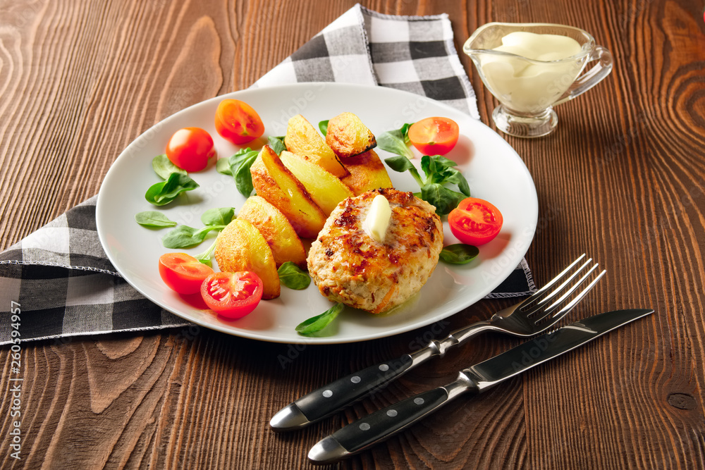 Fried chicken cutlet with potato slices served with tomato cherry and corn salad. Traditional belorussian food - roasted minced meat and potato
