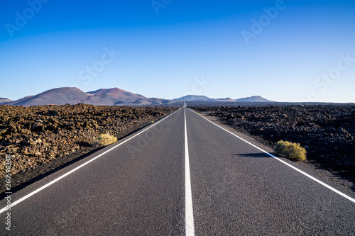 Spain, Lanzarote, Bolt upright endless black asphalt road alongside black lava fields heading to volcanoes