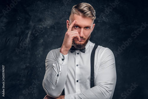 Pensive male thinking about something important. Stylishly dressed young man in shirt with bow tie and suspenders posing with hand on chin.