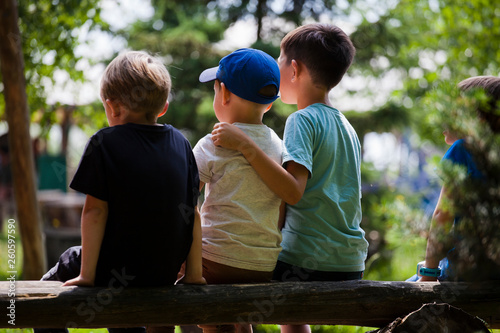 Three boys friends sitting on a log in the summer in the park. Three brothers together