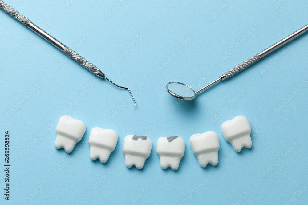 White tooth with caries on blue background and dentist tools mirror, hook. White tooth with caries on blue background and dentist tools mirror, hook.