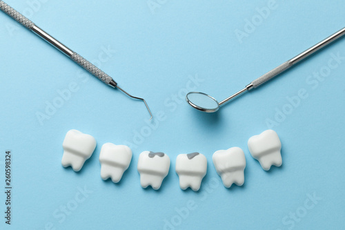 White tooth with caries on blue background  and dentist tools mirror, hook. photo