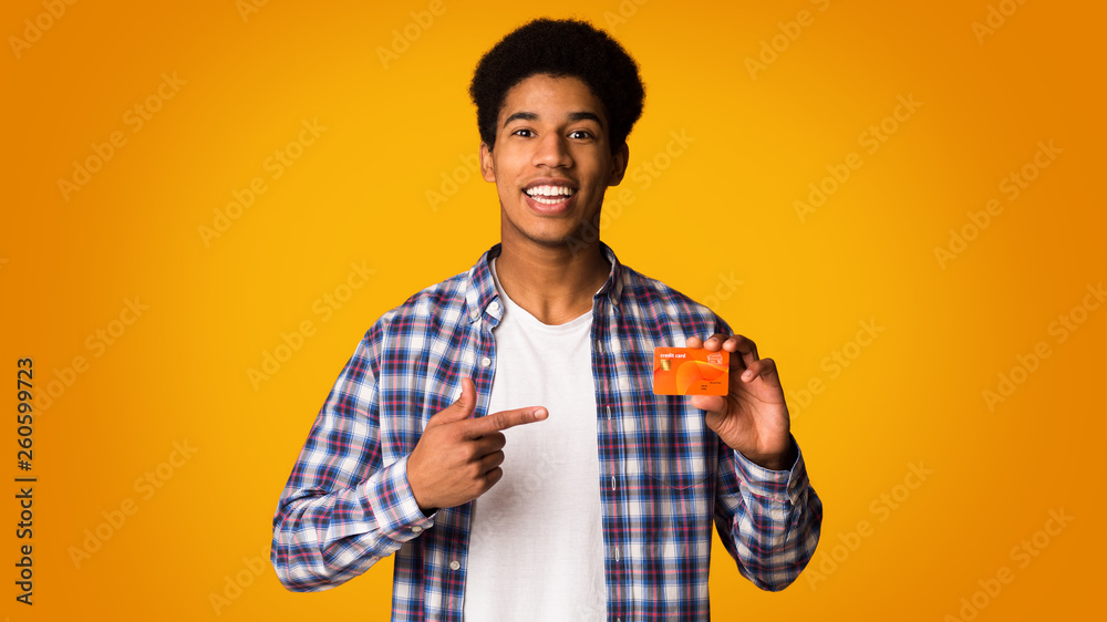 Happy african-american guy holding credit card and point on it Happy african-american guy holding credit card and point on it